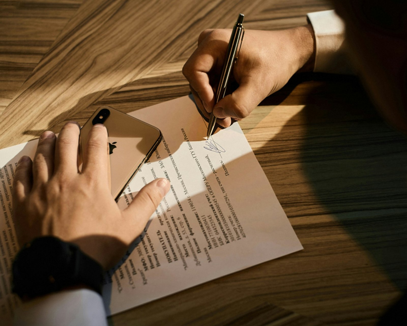 Mano firmando un documento sobre una mesa de madera