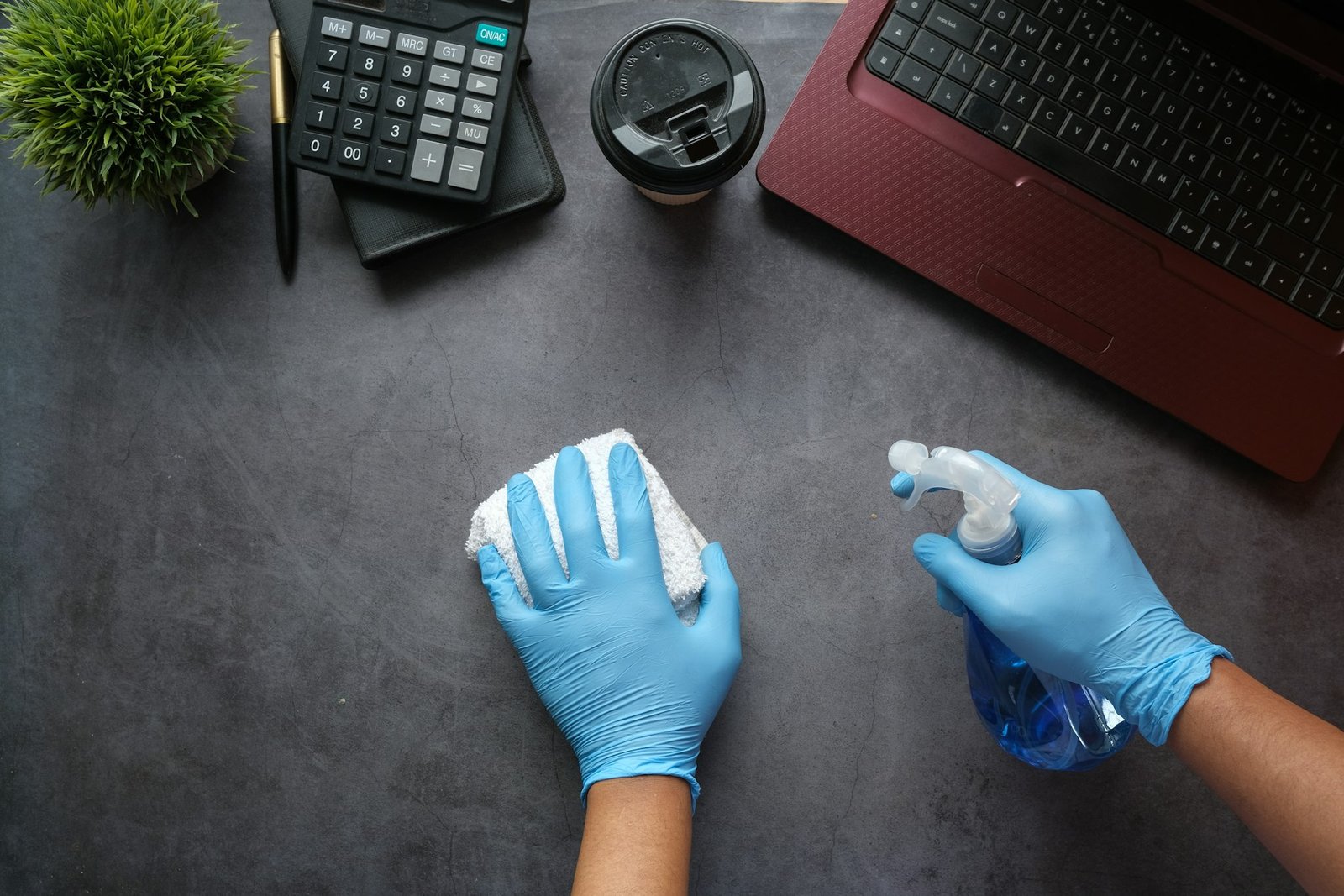 Manos con guantes limpiando un escritorio con un pulverizador