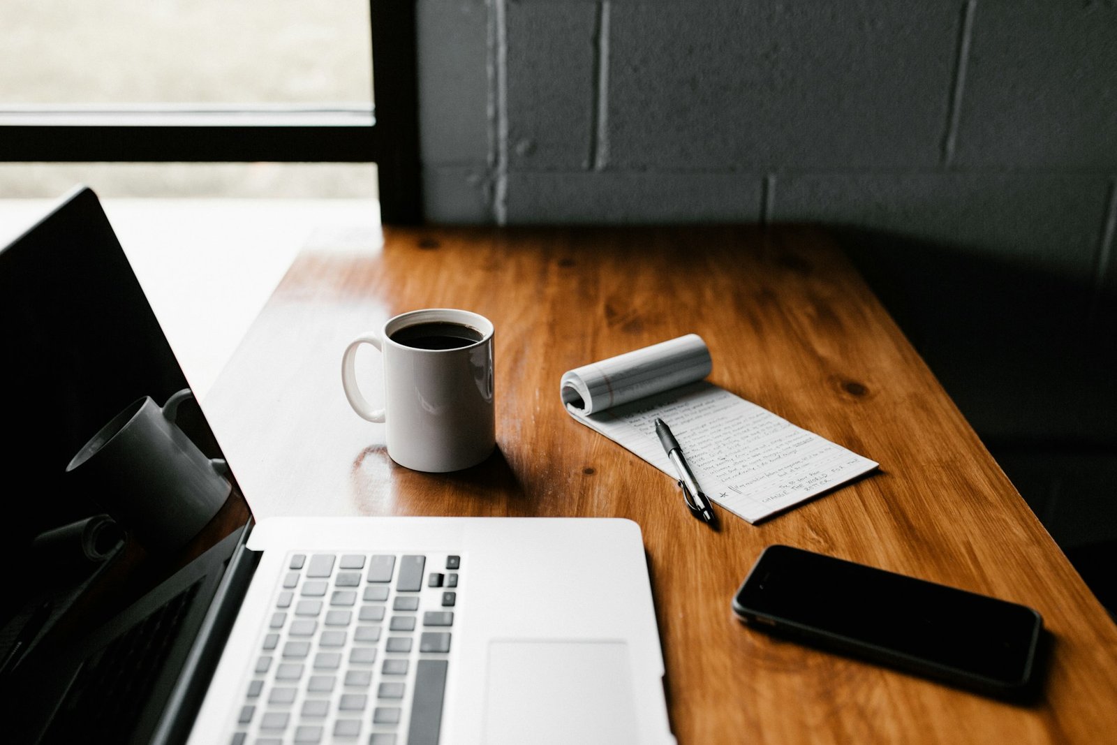 Escritorio de madera con ordenador portátil, taza de café, libreta y teléfono