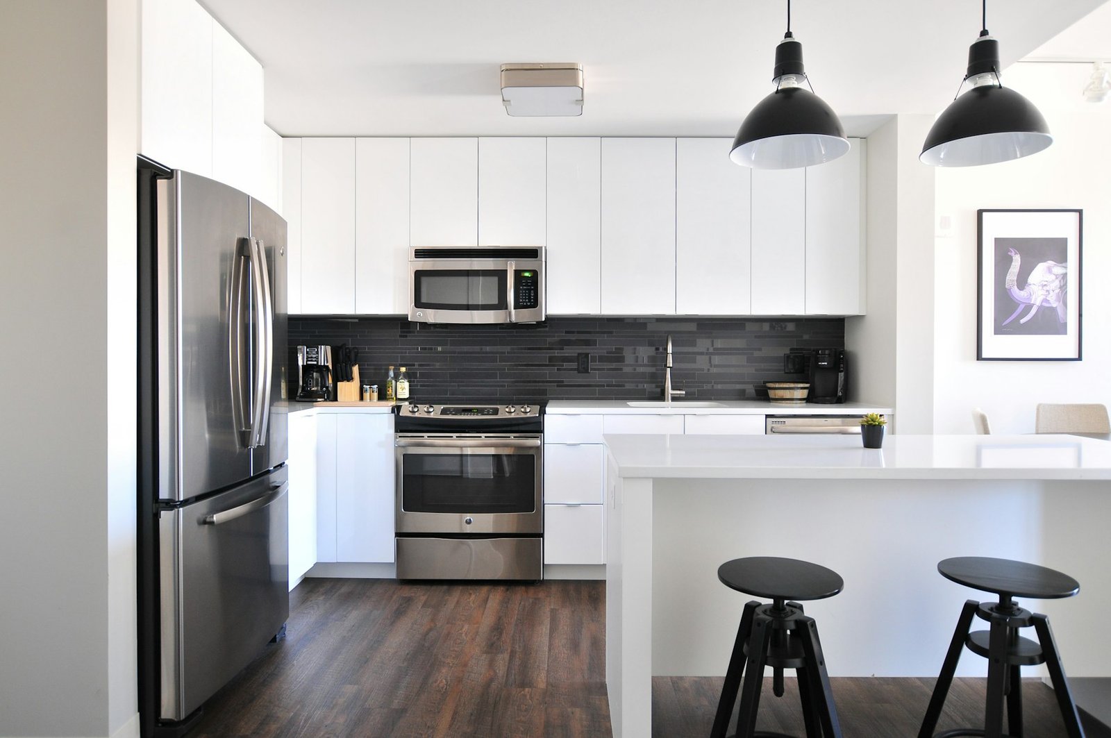 Cocina reformada con muebles blancos, electrodomésticos de acero y lámparas colgantes